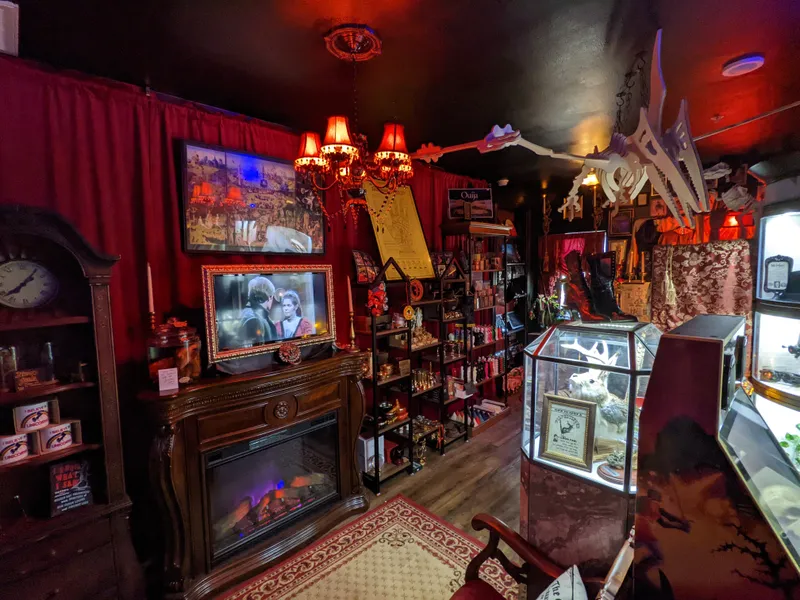 Interior of a dimly lit shop with red curtains, a fireplace, and display cases filled with curios. A dinosaur skeleton hangs from the ceiling.