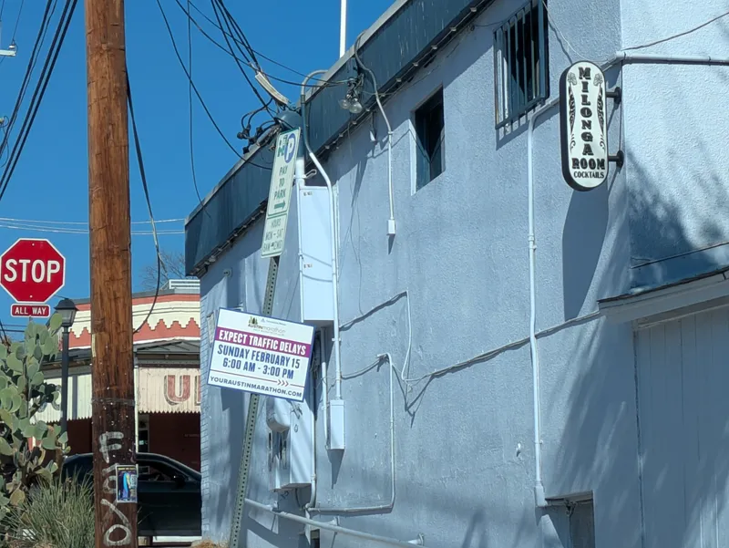 A light blue building with a sign for Milonga Room Cocktails and a traffic sign indicating traffic delays.