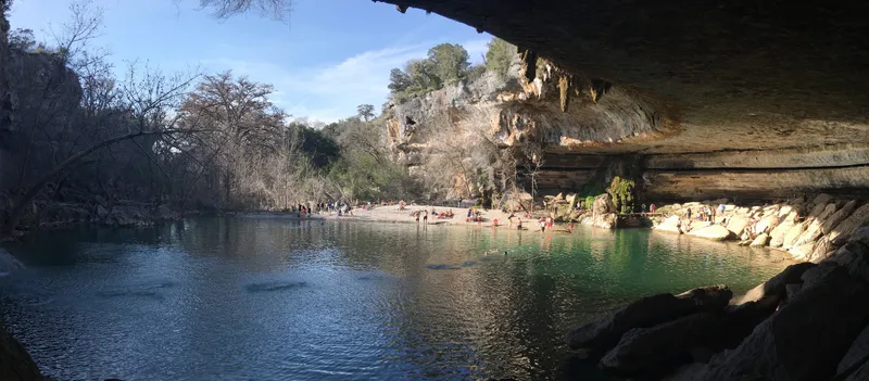 People swimming and relaxing at Hamilton Pool Preserve, a natural grotto with a waterfall and clear green water.