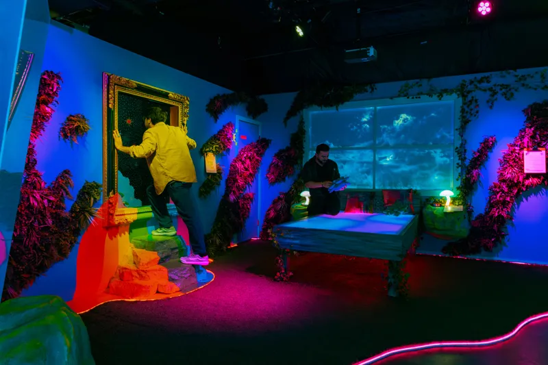 Two people interacting with a surreal, immersive art installation with vibrant neon lighting and fantastical elements.
