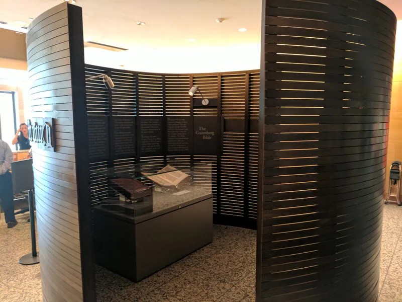 A Gutenberg Bible exhibition features two open Bibles in glass cases within a curved, slatted wooden enclosure.