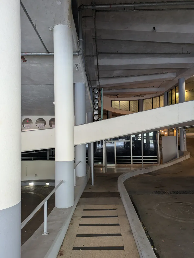 Interior of a multi-level building with concrete columns, ramps, and glass doors.