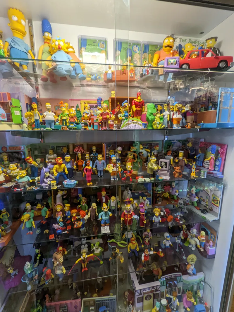 A glass display case filled with many Simpsons action figures, including the Simpson family and various characters.