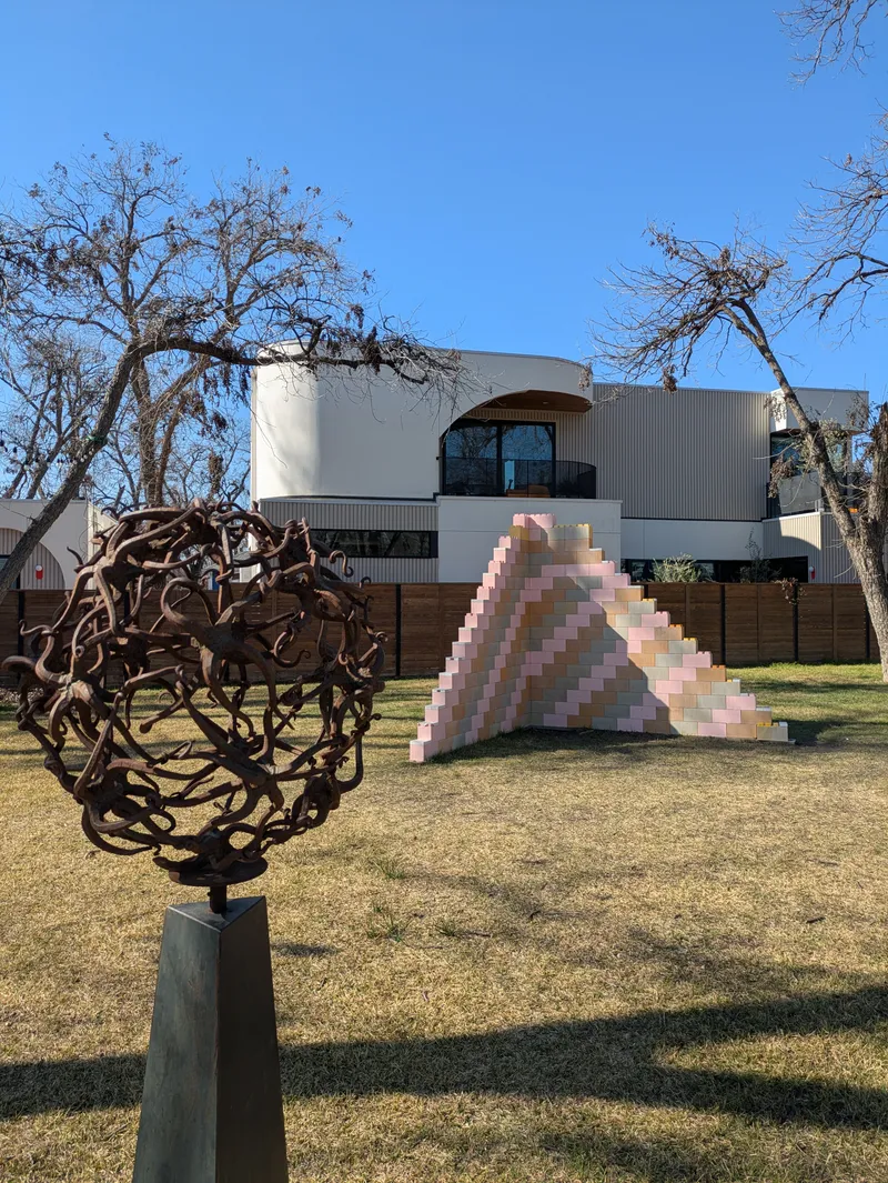 Outdoor sculpture garden with a spherical metal artwork and a stepped, colorful structure.
