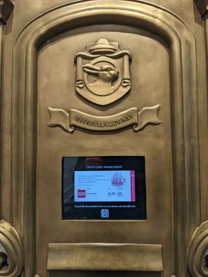 A brass-toned plaque with a shield emblem and "Interimaginary" text above a screen displaying a virtual ticket.