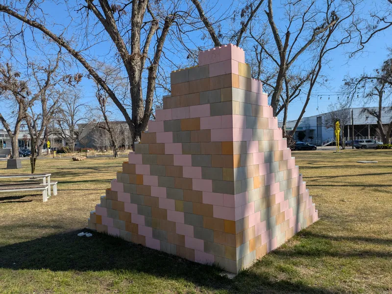 A large, stepped pyramid sculpture made of colorful blocks in a grassy park.