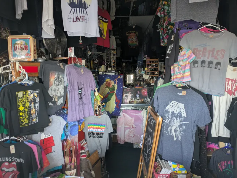 A cluttered retail store interior displaying band t-shirts, novelty items, and various merchandise.