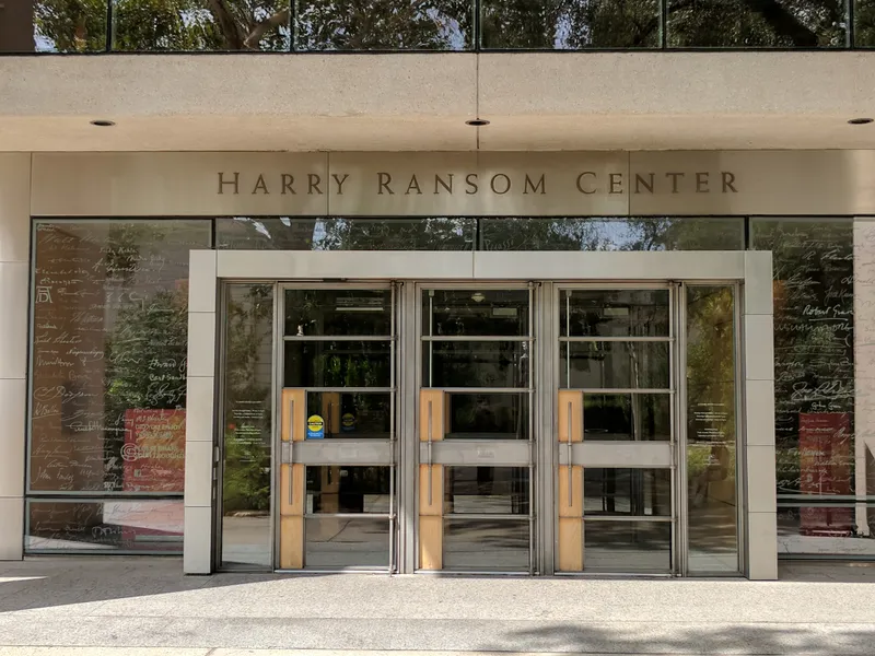 The Harry Ransom Center entrance with glass doors reflecting trees and inscribed names on the facade.