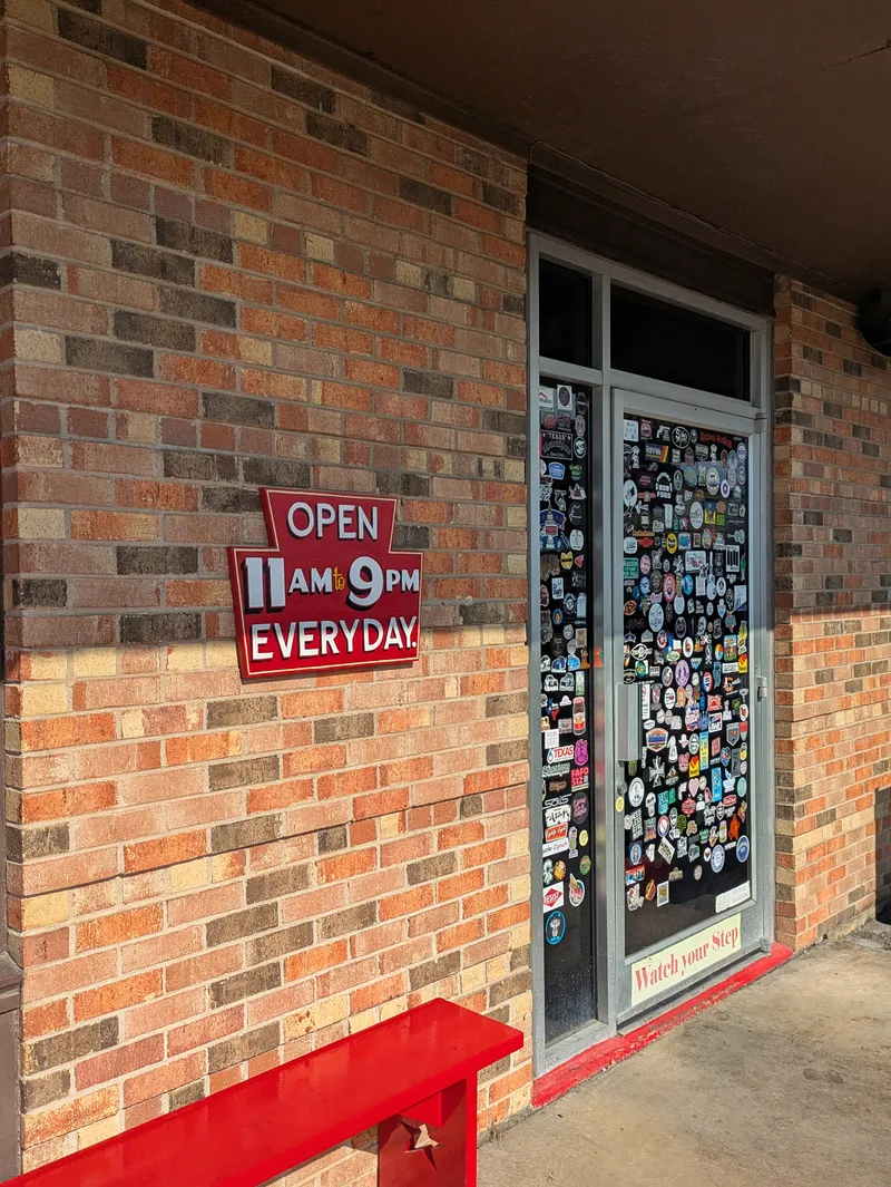 A brick building entrance with a red bench and a glass door covered in stickers.