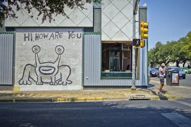 Graffiti art of a frog with the words "HI, HOW ARE YOU" on a building exterior.