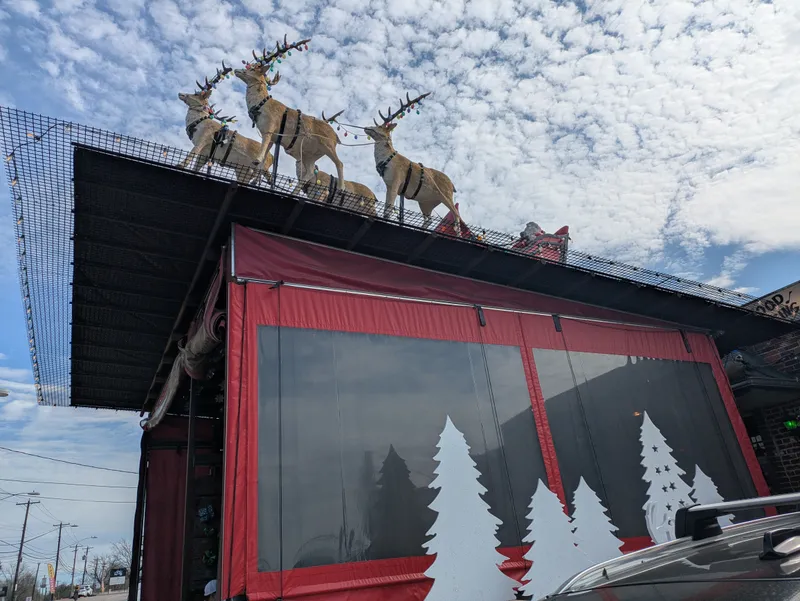 Reindeer decorations on a rooftop with Christmas lights against a cloudy sky.