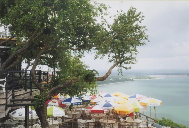 Outdoor seating area with tables and umbrellas overlooking a large body of water.