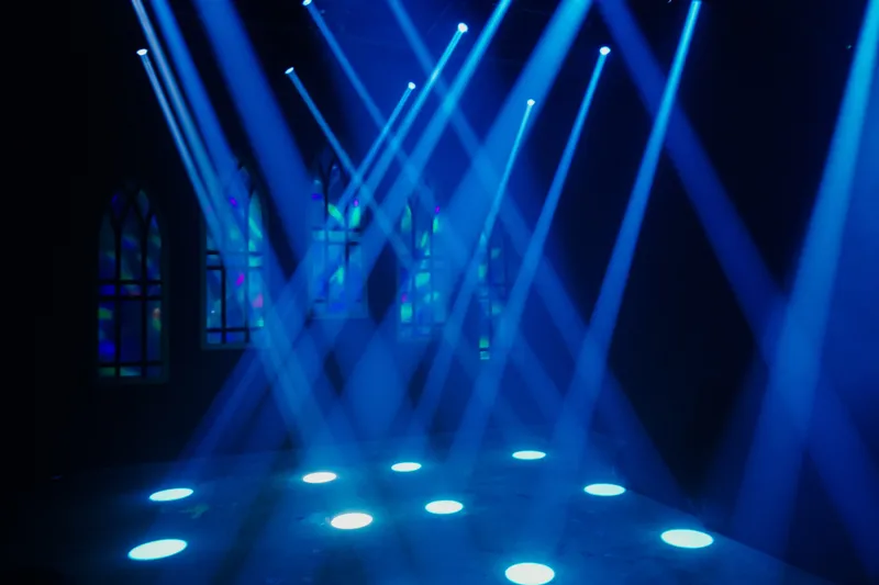 Stage with blue spotlights and illuminated floor lights, with arched windows in the background.