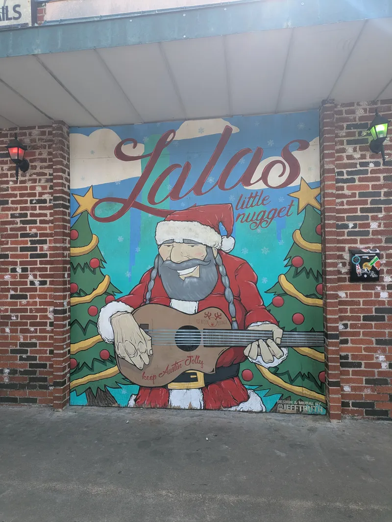 Mural of a Santa Claus character with a beard and braids playing a guitar, with Christmas trees and snowflakes in the background.