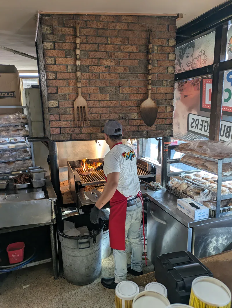 A cook grilling burgers over an open flame in a restaurant kitchen.