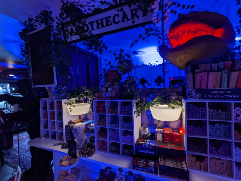 The Curia Arcanum House of Curiosities features an "APOTHECARY" sign, shelves stocked with incense, and a large, carved object glowing red.