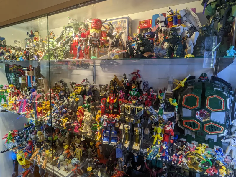 A glass display case overflowing with vintage action figures, including Power Rangers, Gundam robots, and Godzilla.