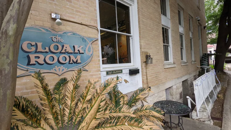 The Cloak Room sign on a brick building with a palm plant in the foreground.