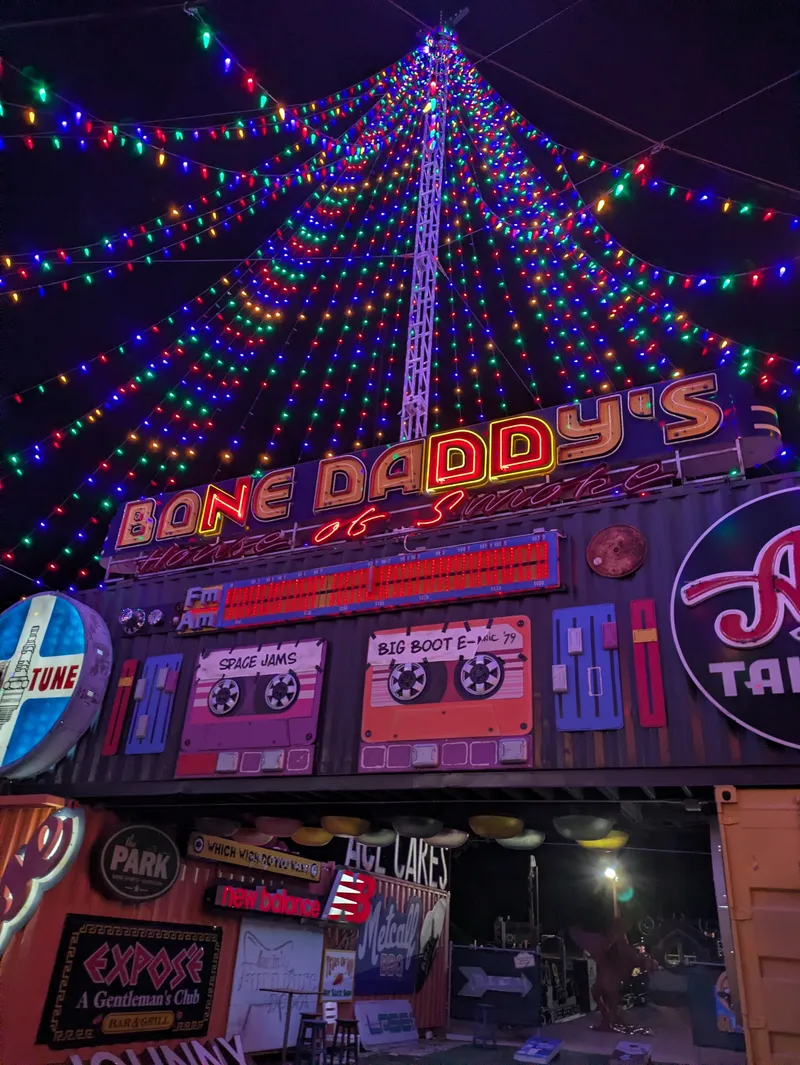 Bone Daddy's House of Smoke restaurant exterior at night, decorated with colorful string lights and retro cassette tape art.