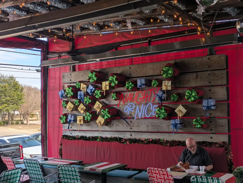 Man eating pizza at a table decorated for Christmas with presents and neon signs.