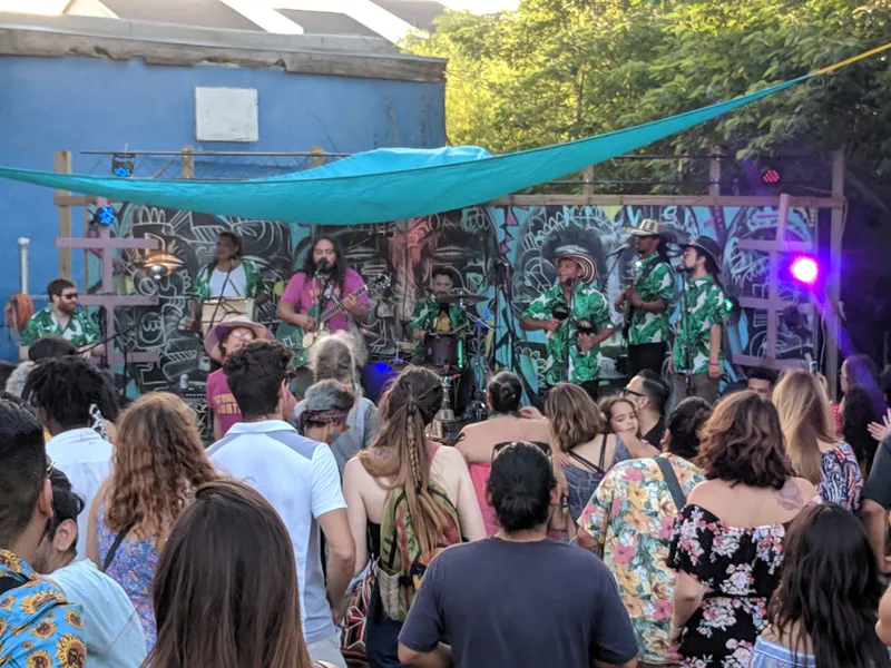 A band performs on an outdoor stage with a colorful mural backdrop, while a crowd watches.