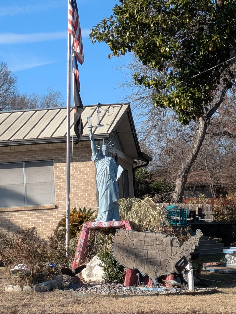 Statue of Liberty replica in a yard with an American flag and a map of the USA.