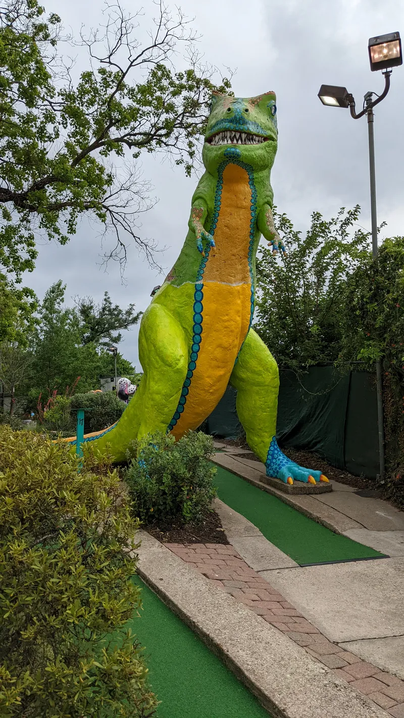 A large, brightly colored dinosaur statue at a mini-golf course.