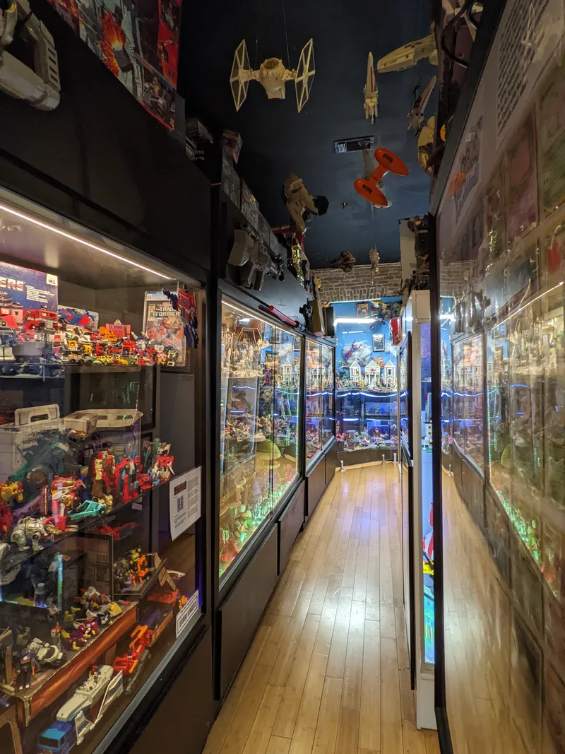 A museum hallway filled with glass display cases overflowing with 80s and 90s action figures and toys, with Star Wars ships hanging from the ceiling.