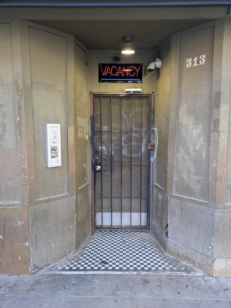 A neon VACANCY sign above a barred door with a checkered tile entryway.