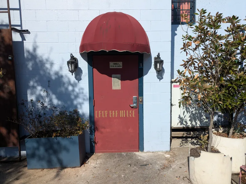 Red door with a marquis awning and "DROP BAR IN USE" text, next to a tree.