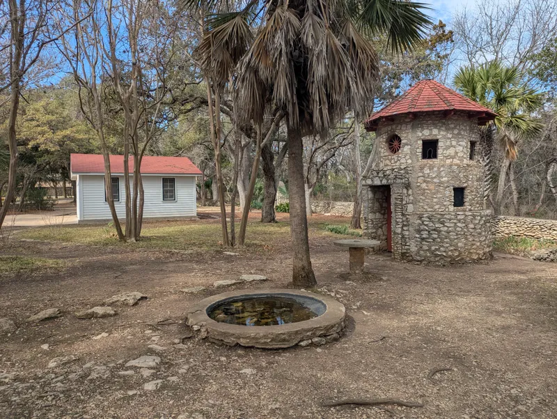 A stone tower with a red roof and a small white building with a red roof in a wooded area.