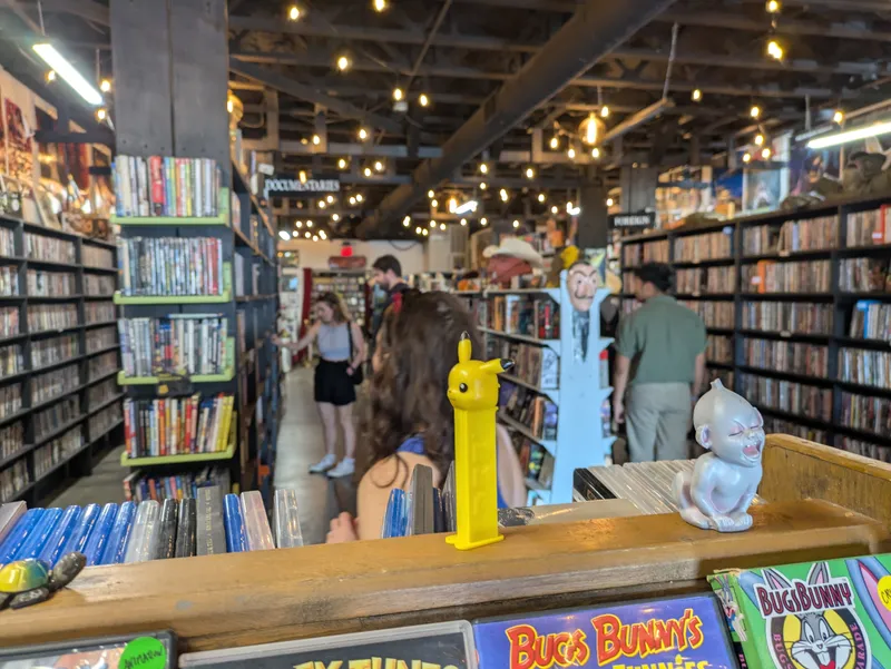 Interior of a store selling DVDs and Blu-rays, with shelves stocked full of cases and a few patrons browsing.