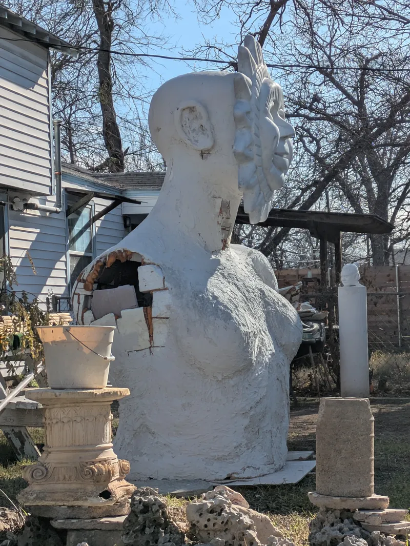 A large, white, unfinished sculpture of a female torso and head with exposed interior.