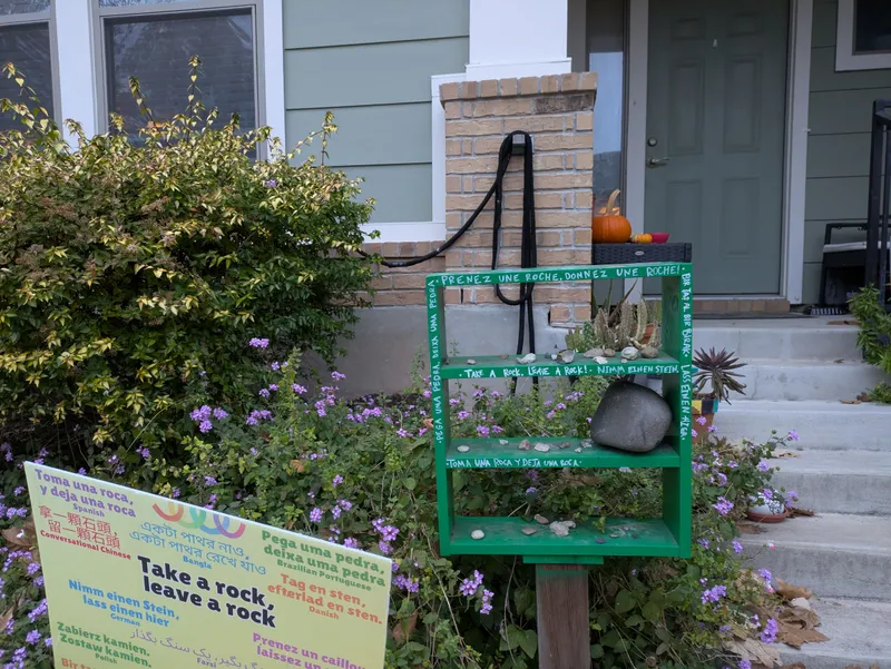 A green shelf display with rocks and plants, featuring multilingual phrases about taking and leaving rocks.
