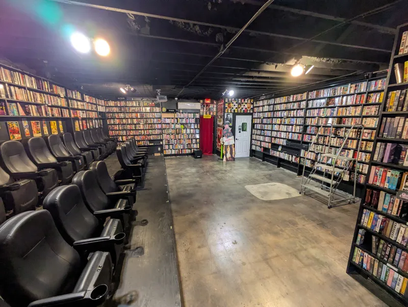 Interior of a video rental store with rows of VHS tapes and theater-style seating.