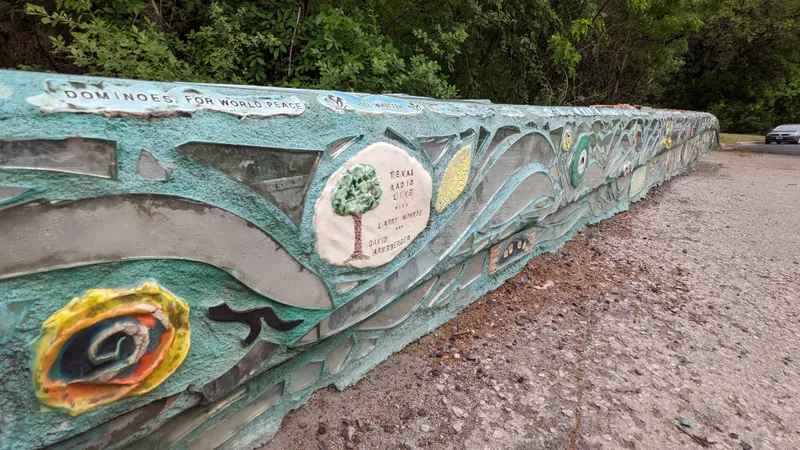 A long, curved wall covered in a mosaic of blue, teal, and reflective pieces, with ceramic art and text.