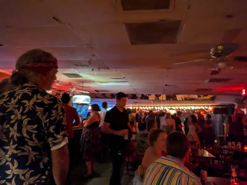 A crowded bar interior with people socializing and dancing under dim lighting and string lights.