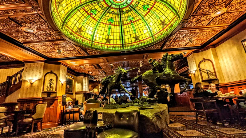 Interior of a grand lobby with a large stained-glass dome and equestrian statues.
