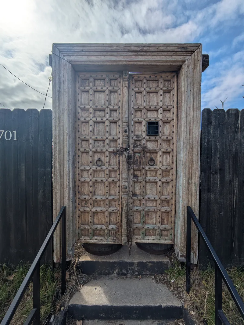 Ornate wooden double doors with metal studs and a small barred window, set within a weathered wooden frame.