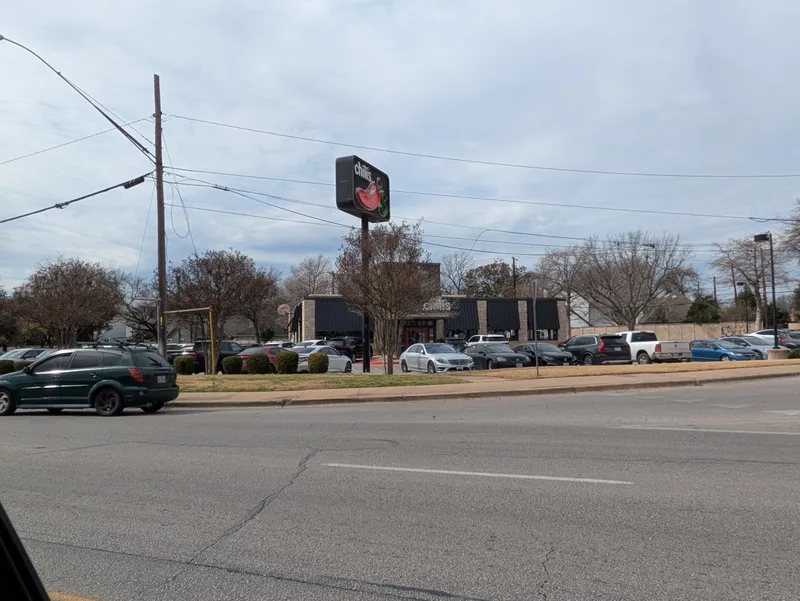 Chili's restaurant exterior with a prominent sign and a parking lot full of cars.