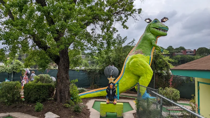 A large, bright green dinosaur statue with a blue and orange tail, part of a mini-golf course.