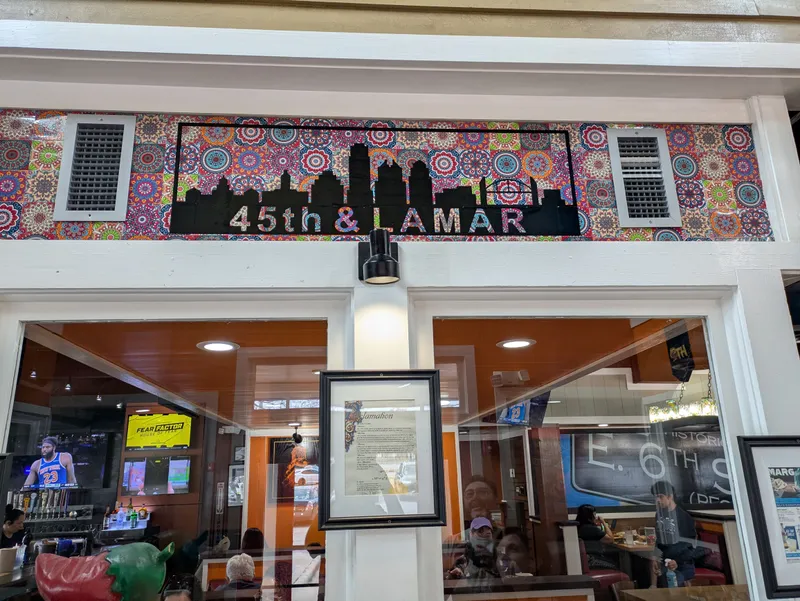 Colorful wall art with a city skyline and "45th & Lamar" text above a restaurant interior.